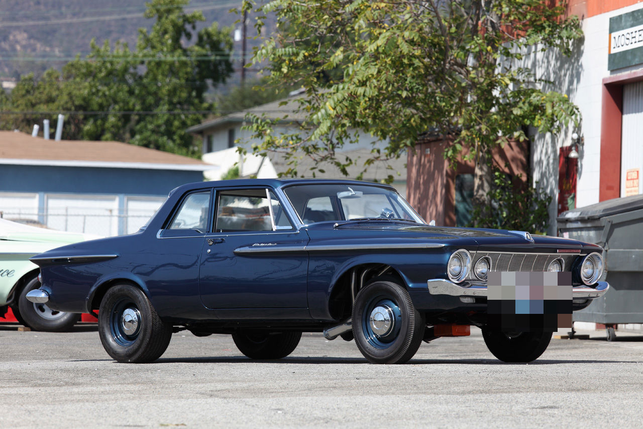 Dark blue 1962 Plymouth Belvedere two-door post sedan with the 1962 grille and small hubcaps, parked outside a shop