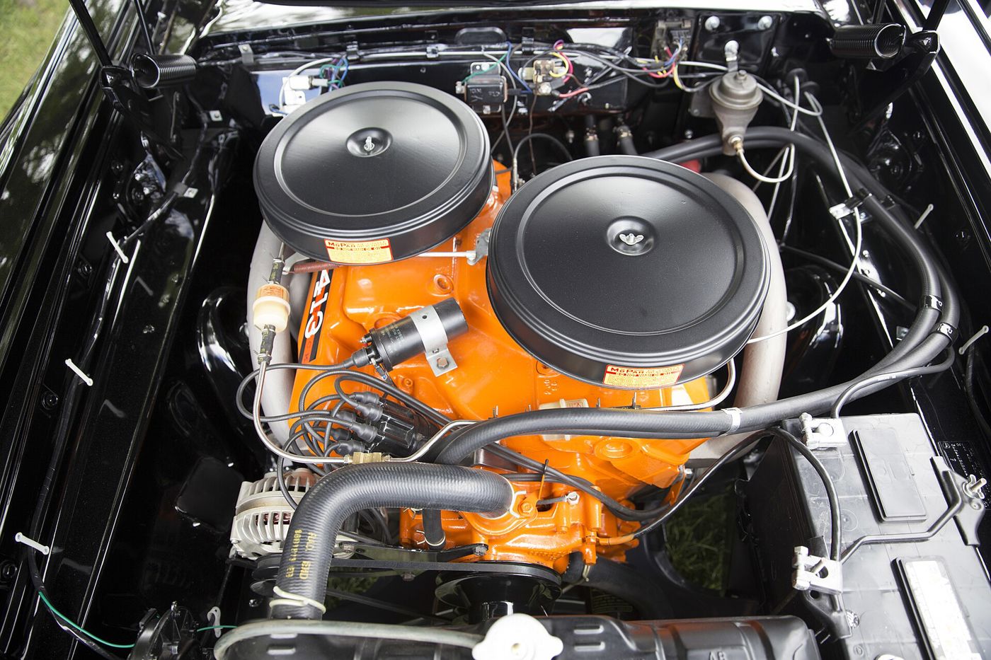 Orange 413 Super Stock V8 with two large black air cleaners on the cross-ram intake, in a black 1962 Plymouth engine bay
