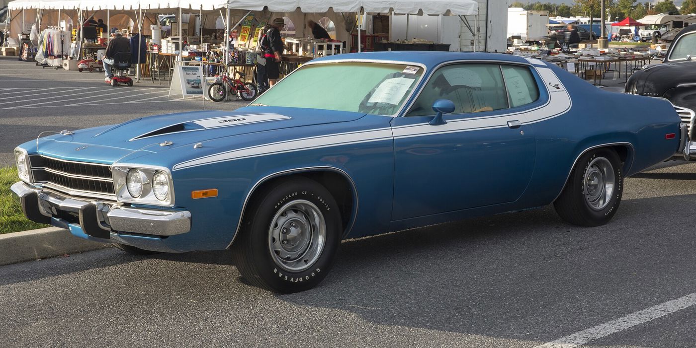 Lucerne Blue 1974 Plymouth Road Runner with white stripes and hood callout, front three-quarter in a car-show field