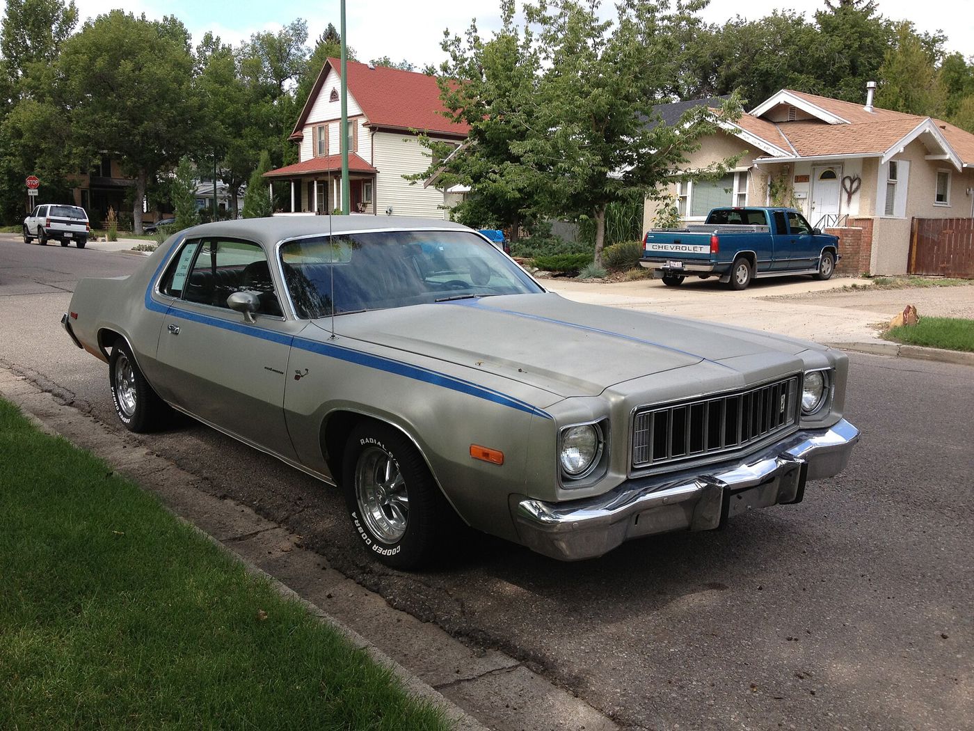 Silver 1975 Plymouth Road Runner with blue side stripes, parked at a kerb in a residential street