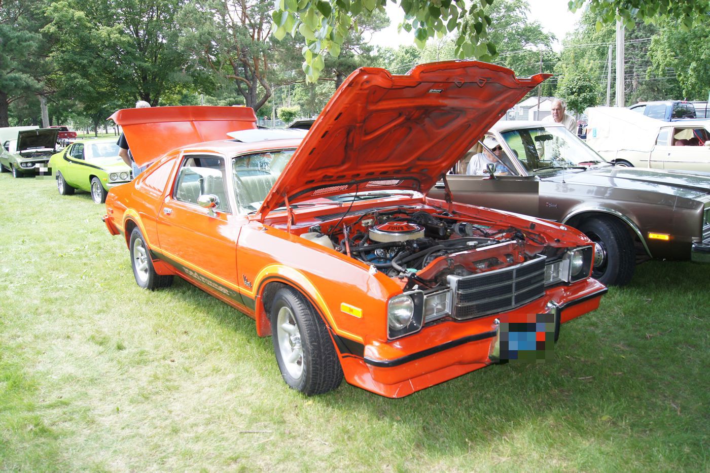 Orange 1977 Plymouth Volare Road Runner with black stripes and the hood raised, on grass at a car show