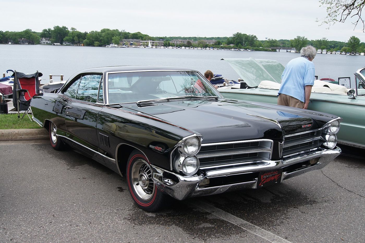Black 1965 Pontiac Catalina 2+2 hardtop with stacked headlamps, 2+2 grille badge, 421 front-fender emblem and redline tires, front three-quarter beside a lake
