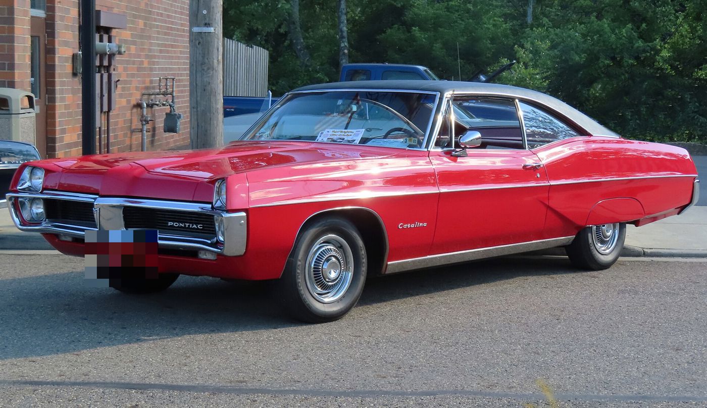 Red 1967 Catalina hardtop coupe with a white roof and stacked headlights, seen from the front three-quarter on a street