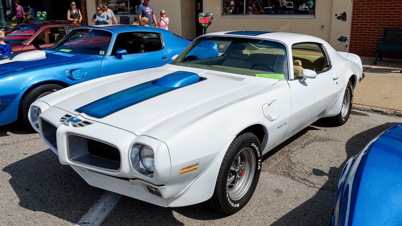 White 1970 Pontiac Firebird Trans Am with blue hood stripe, shaker hood scoop and Trans Am fender script, front three-quarter at a street car show