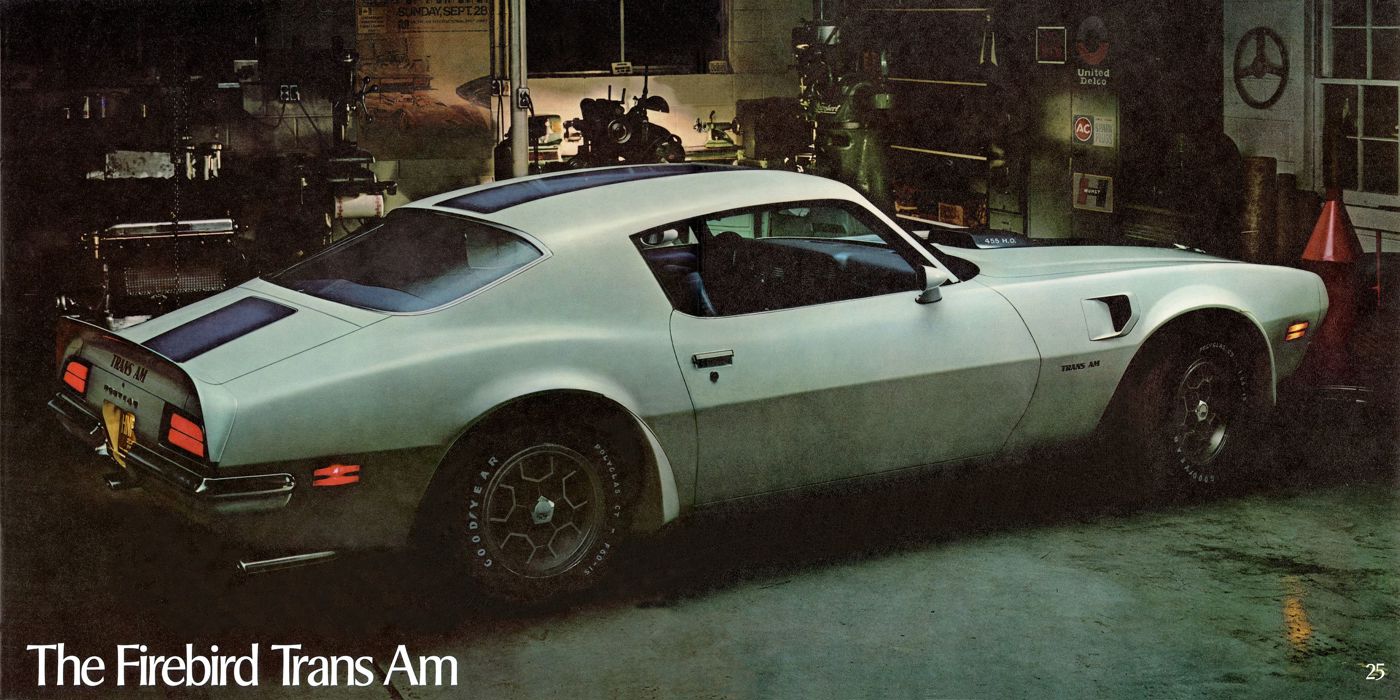 White 1971 Firebird Trans Am with blue stripe, shaker hood and rear spoiler, seen from the rear three-quarter in a garage