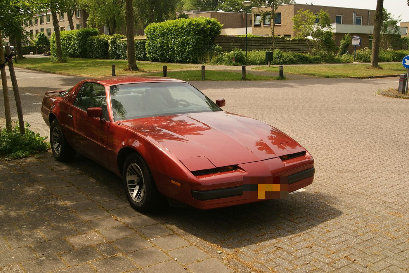 Red 1989 Firebird with hidden headlamps, front three-quarter on a brick-paved square in the Netherlands