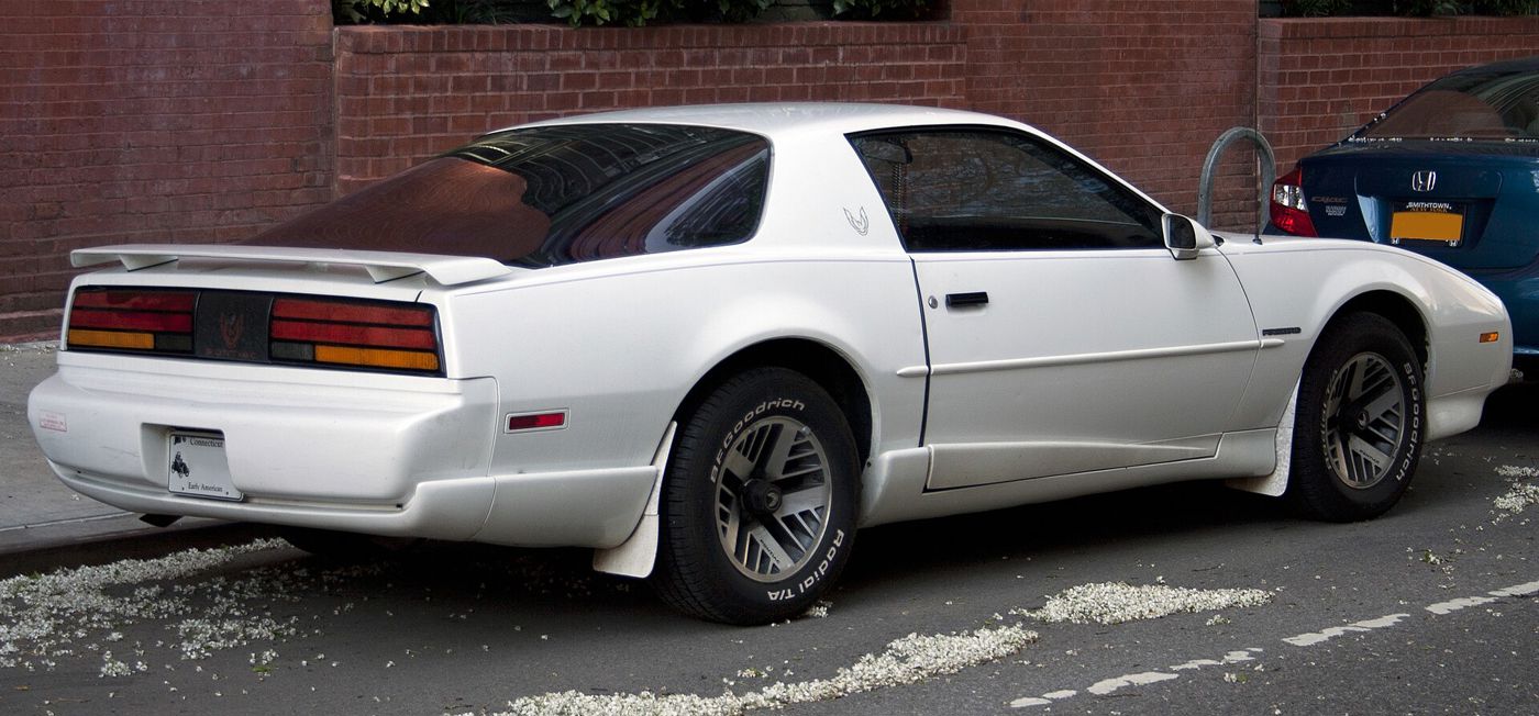 White 1992 Firebird from the rear three-quarter, showing its spoiler and full-width taillamps, parked at a curb