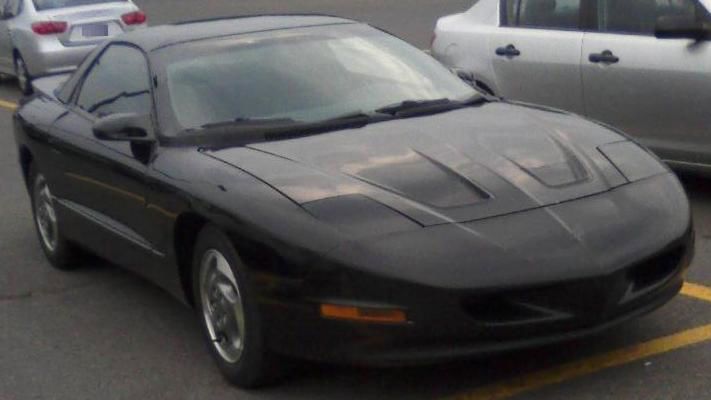Black fourth-generation Firebird with its pointed nose and pop-up headlamps, front three-quarter in a parking lot