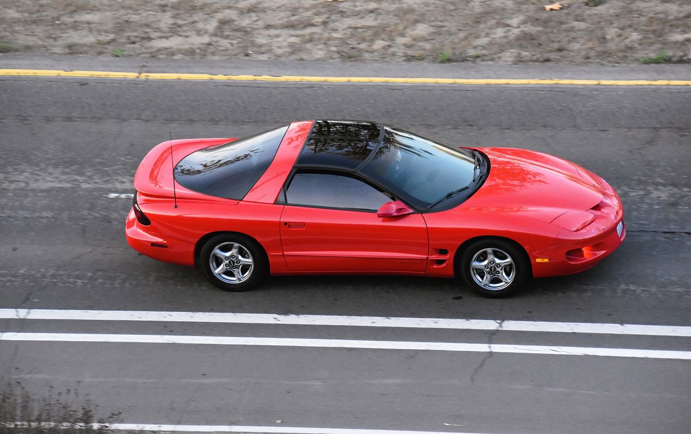 Red 1999 Firebird Formula with a black T-top roof seen from above in side view on a road