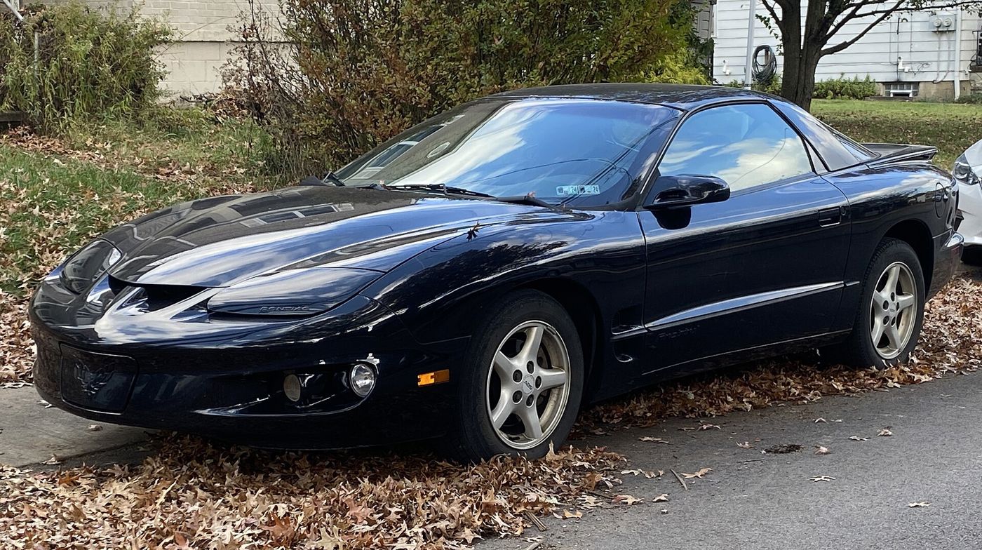 Black 2001 Firebird coupe front three-quarter at a curb covered with autumn leaves