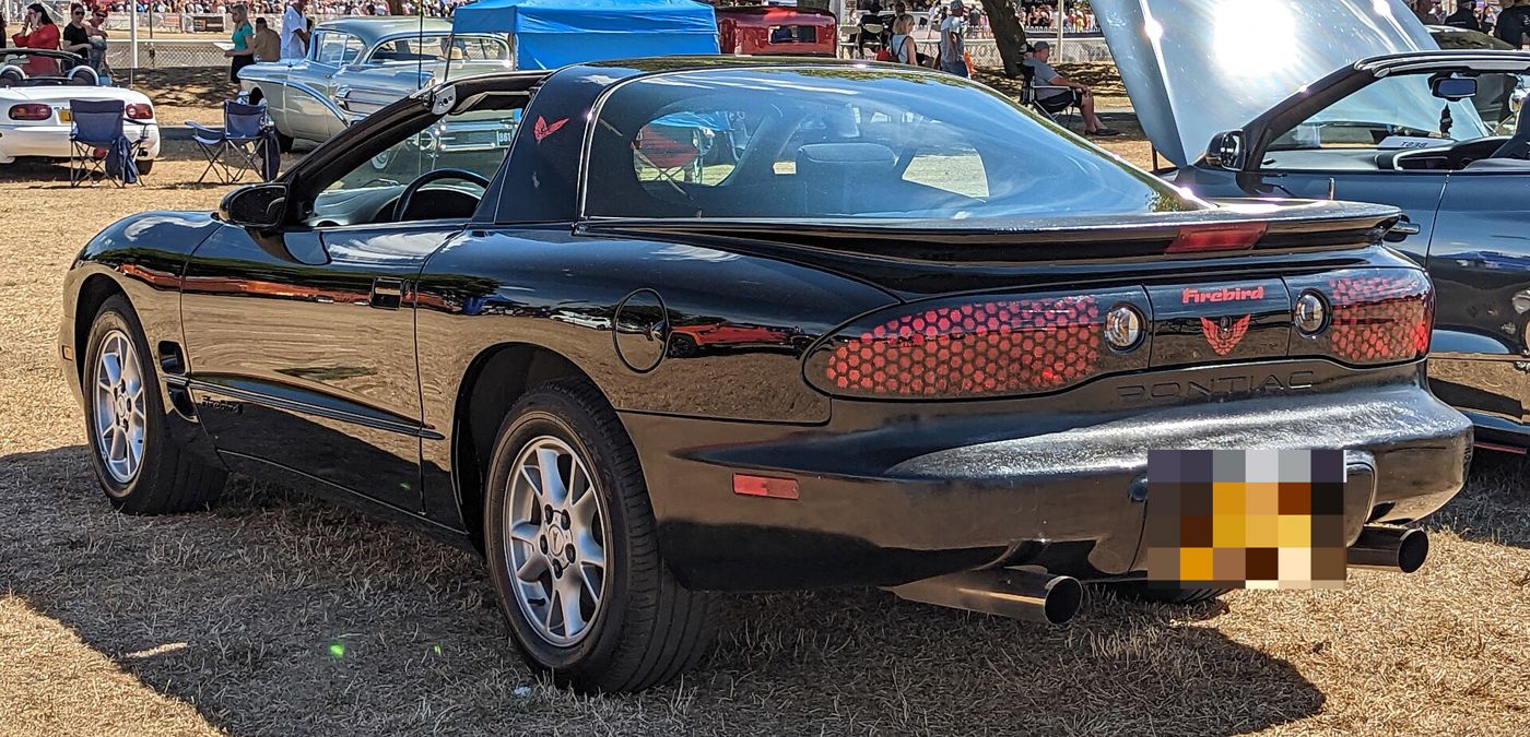 Black 2002 Firebird from the rear three-quarter, showing honeycomb taillamps and twin exhausts, at a grass car show