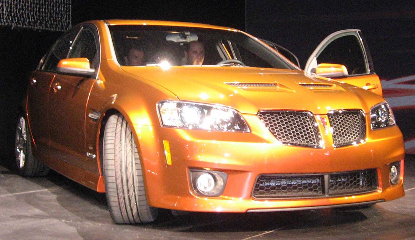 Bright orange 2009 G8 GXP sedan on an auto-show stand, front three-quarter, with its GXP front fascia and hood vents