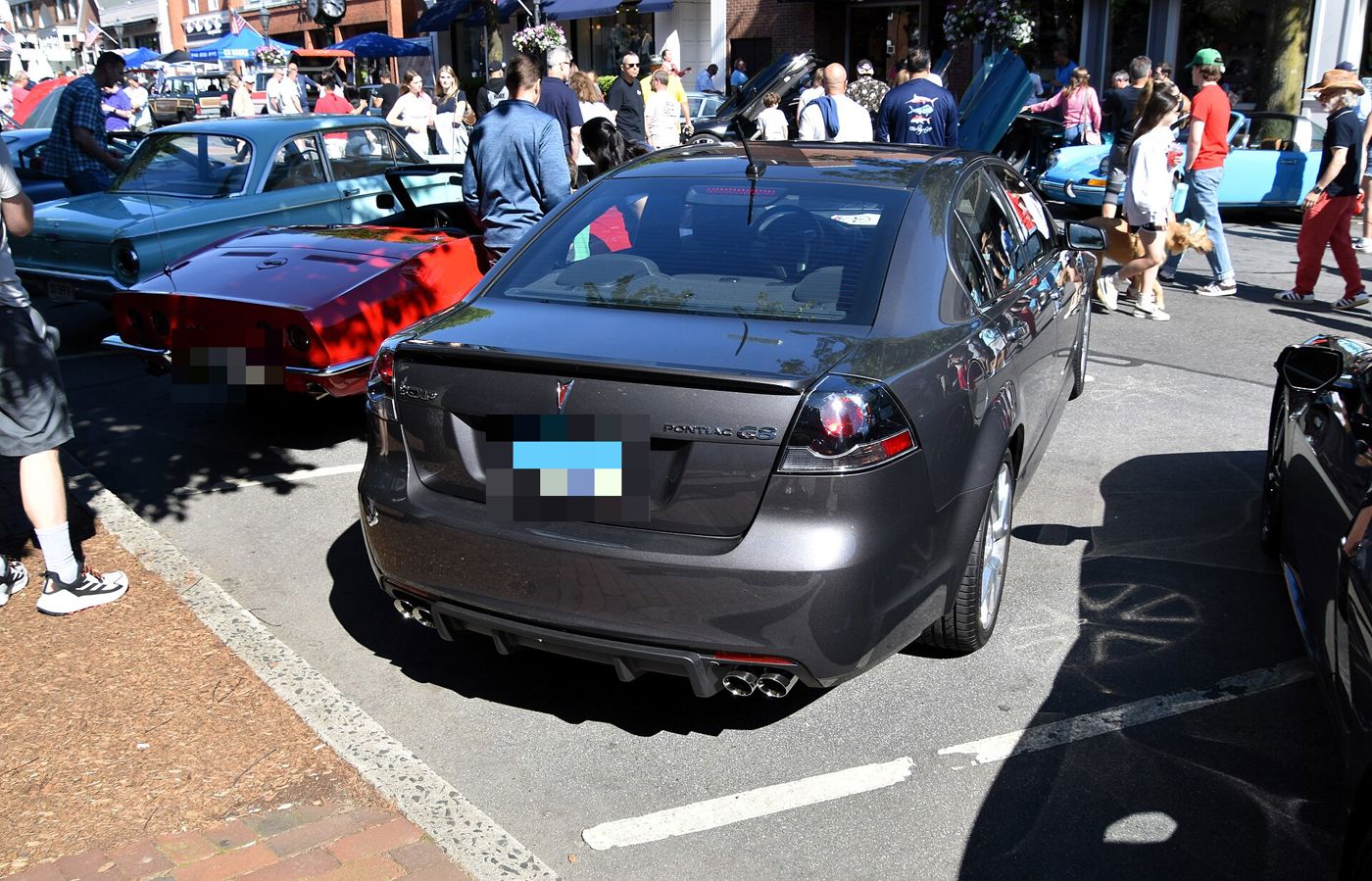 Rear view of a gray 2009 G8 GXP showing its decklid spoiler, taillamps and four exhaust outlets, parked at a crowded street car show