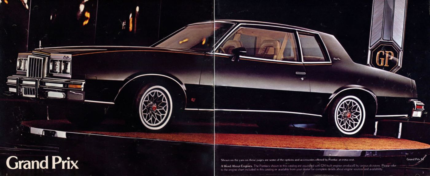 Black 1978 Grand Prix coupe in side view on a dark stage beside a large GP emblem