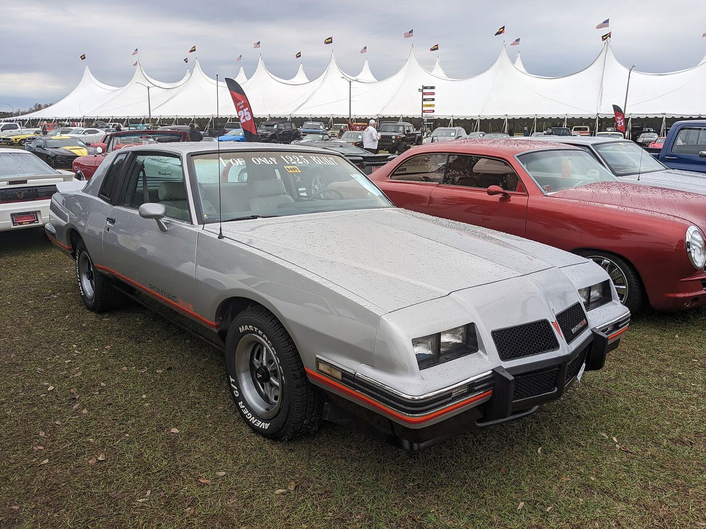 Silver 1986 Grand Prix 2+2 with its aero nose and bubble back window, red lower stripe, front three-quarter on grass at an auction