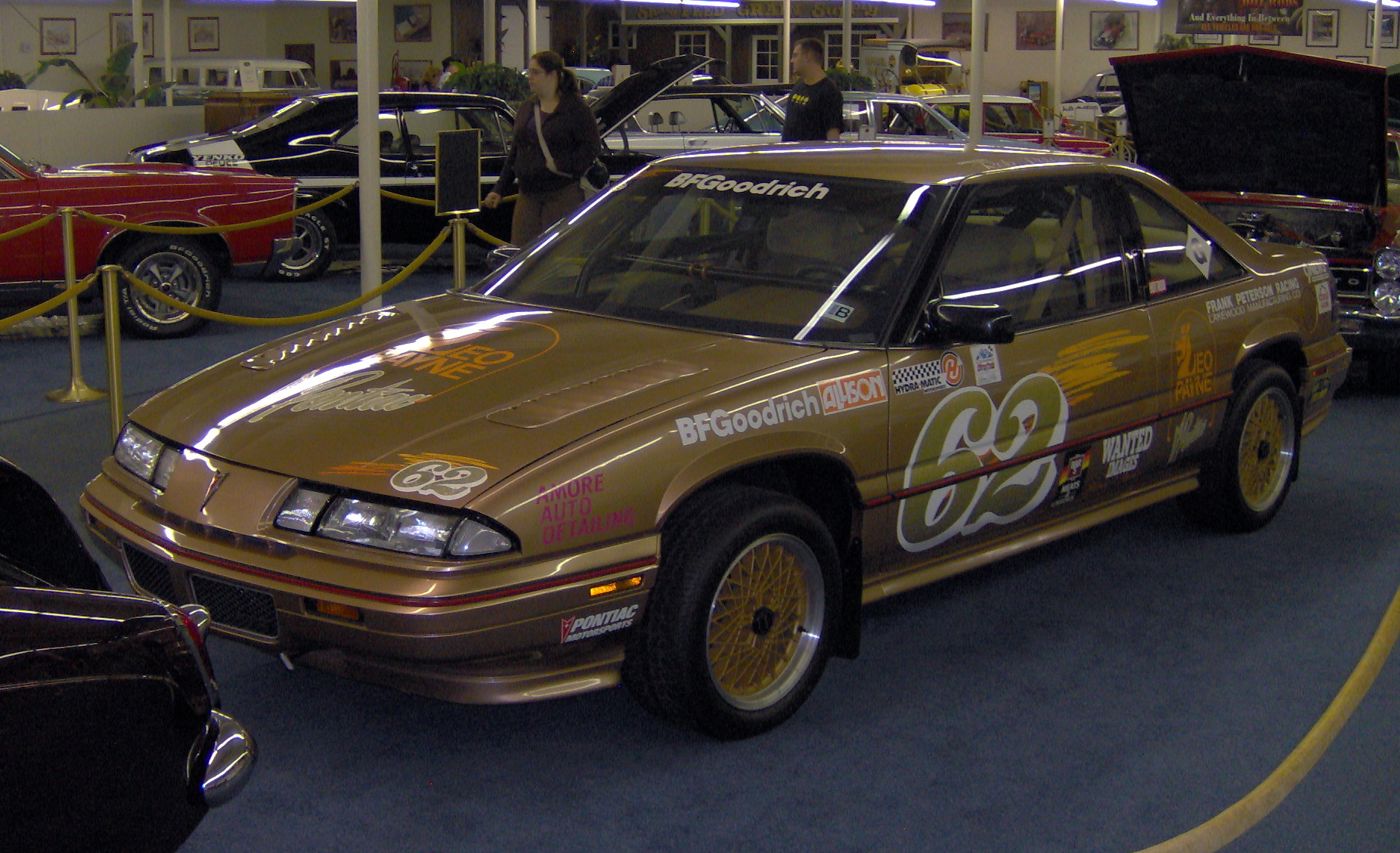Gold 1988 Grand Prix race car with number 63 and sponsor decals, displayed behind rope barriers in a museum