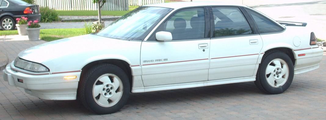 White Grand Prix four-door sedan with red pinstripe in side view on a paved lot