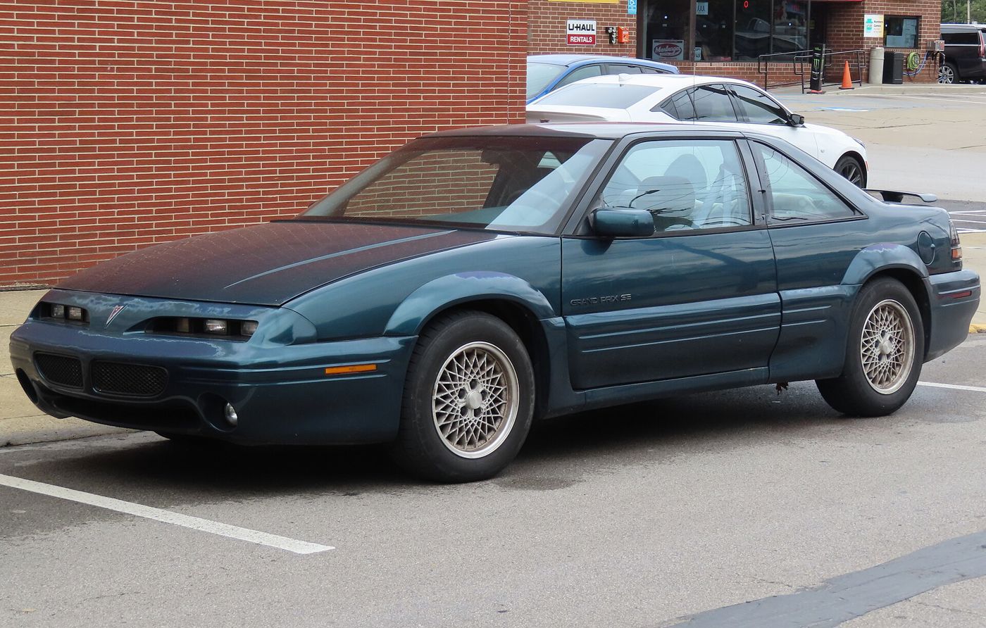Teal 1996 Grand Prix SE coupe with lattice wheels, front three-quarter by a brick wall