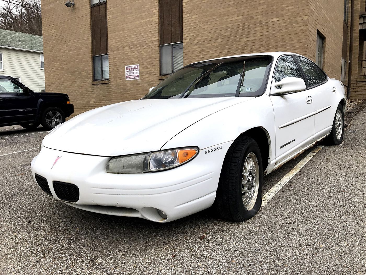 White 1998 Grand Prix sedan front three-quarter in a parking lot beside a brick building