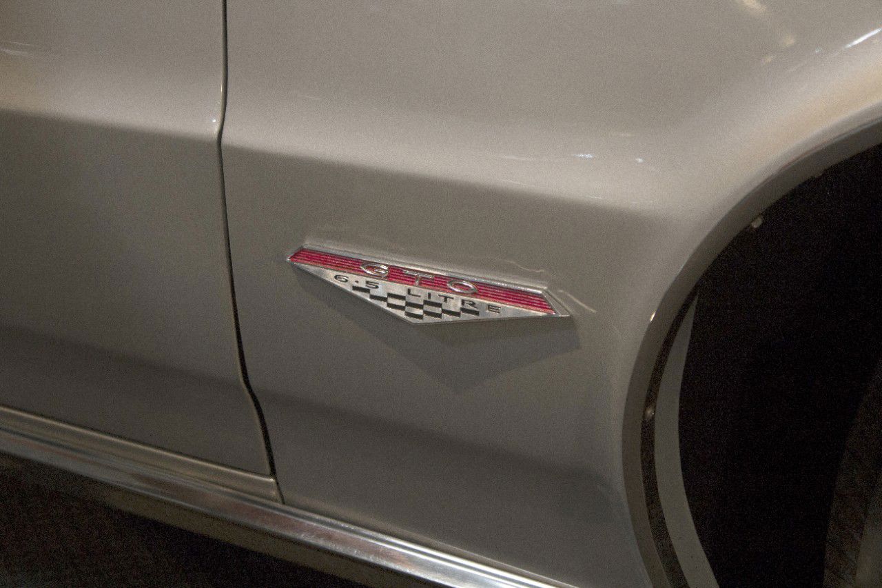 Close-up of the triangular red, chrome and checkered GTO 6.5 LITRE badge on the silver front fender of a 1964 GTO