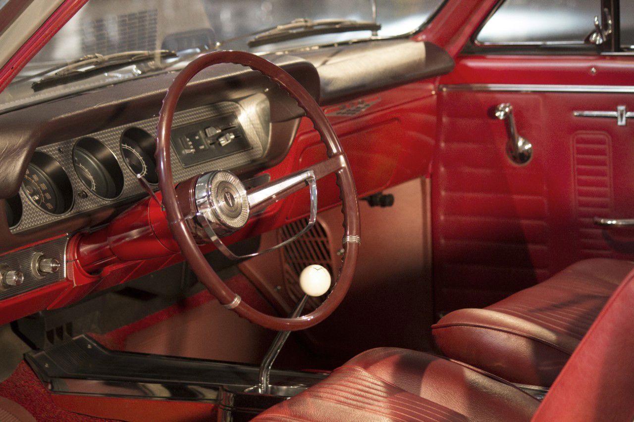 Red interior of a 1964 GTO with a thin-rim steering wheel, engine-turned dash panel with round gauges, bucket seats and a white shift knob