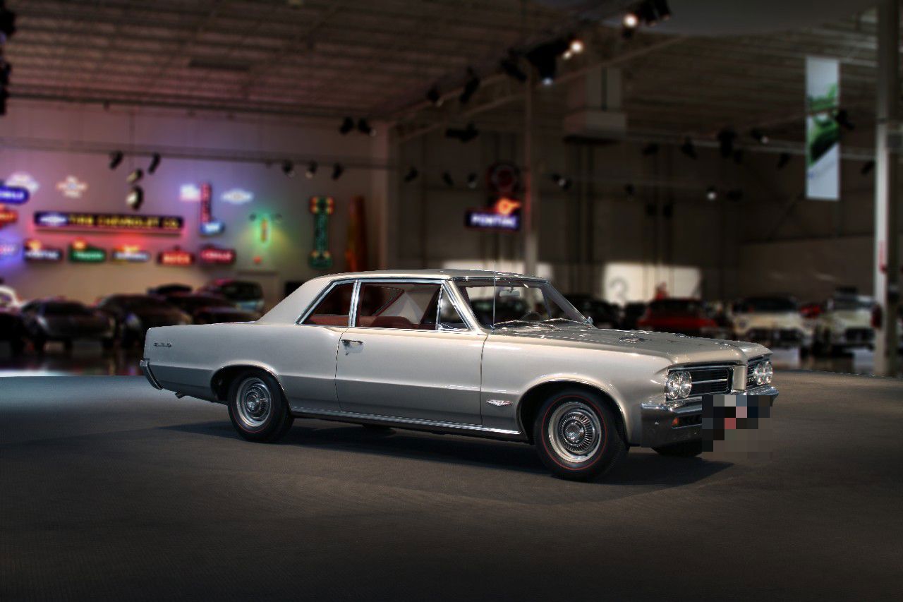 Silver 1964 Pontiac GTO two-door coupe with split grille and stacked-look headlamps, front three-quarter in the GM Heritage Center hall