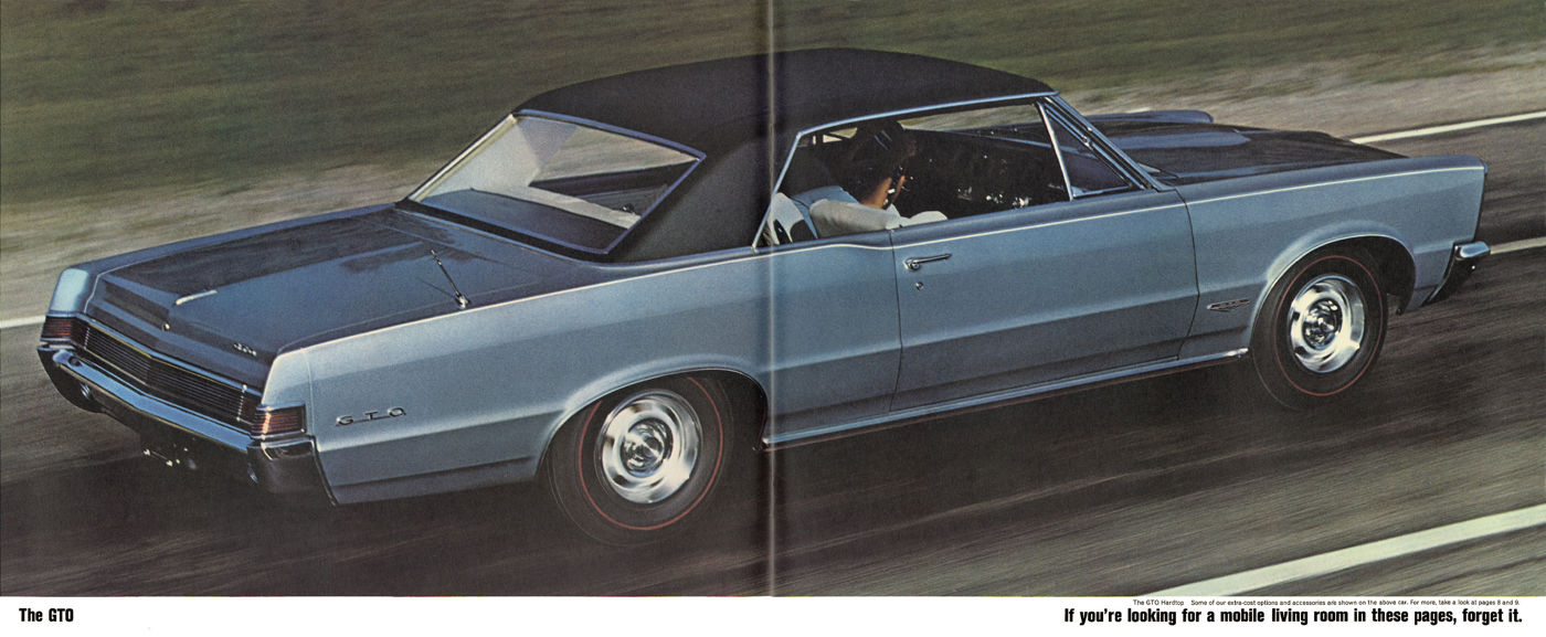 Blue 1965 GTO hardtop with a black vinyl roof driving on a road, rear three-quarter view