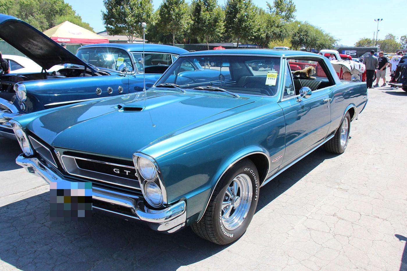 Turquoise 1965 GTO hardtop with vertically stacked headlamps, hood scoop and GTO grille lettering, front three-quarter at a car show