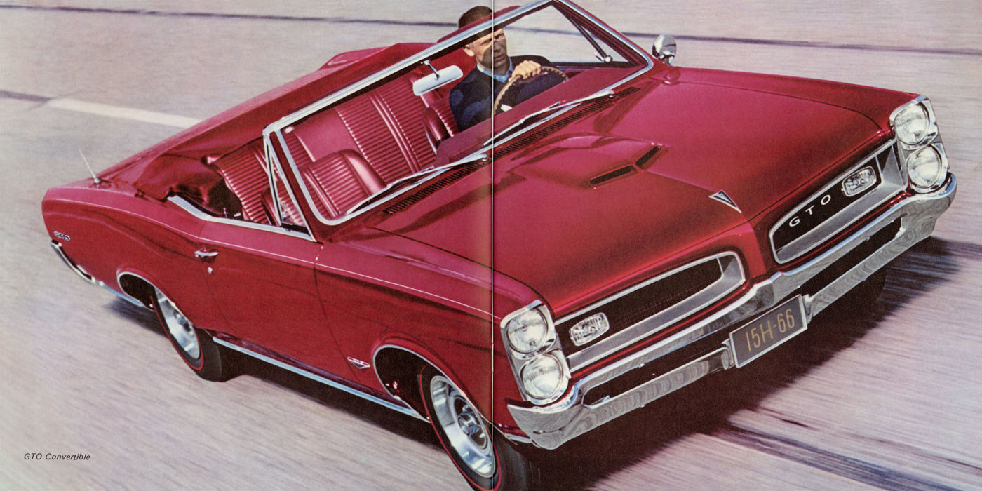 Red 1966 GTO convertible with the top down, high front three-quarter view on a road, a driver at the wheel
