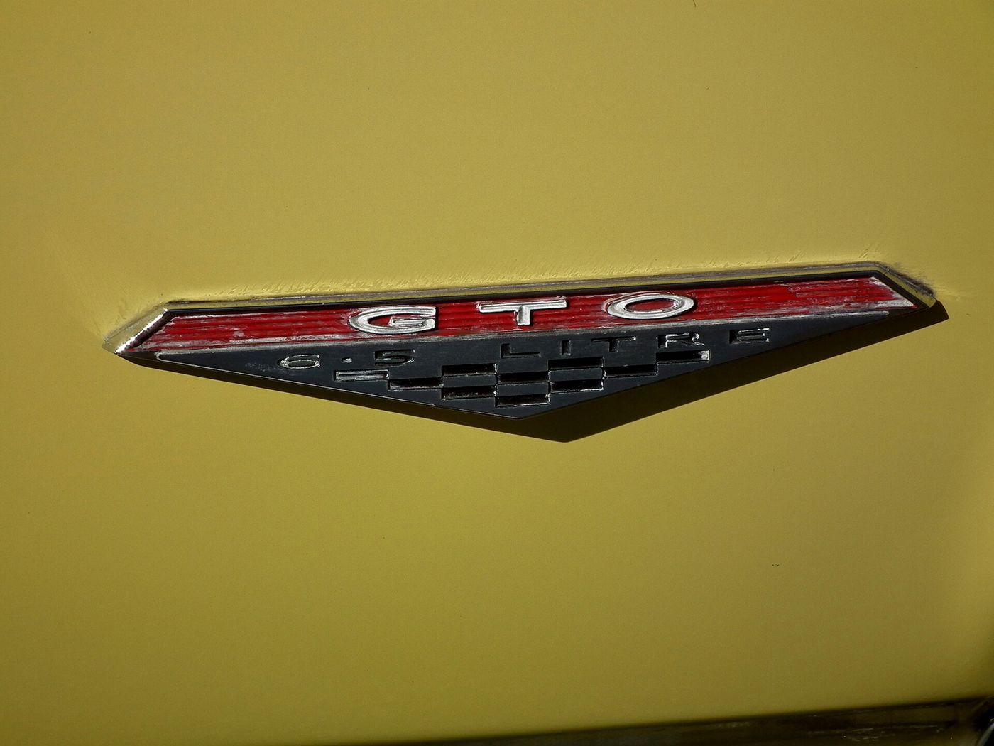 Close-up of the GTO 6.5 LITRE fender badge on the yellow front fender of a 1966 GTO