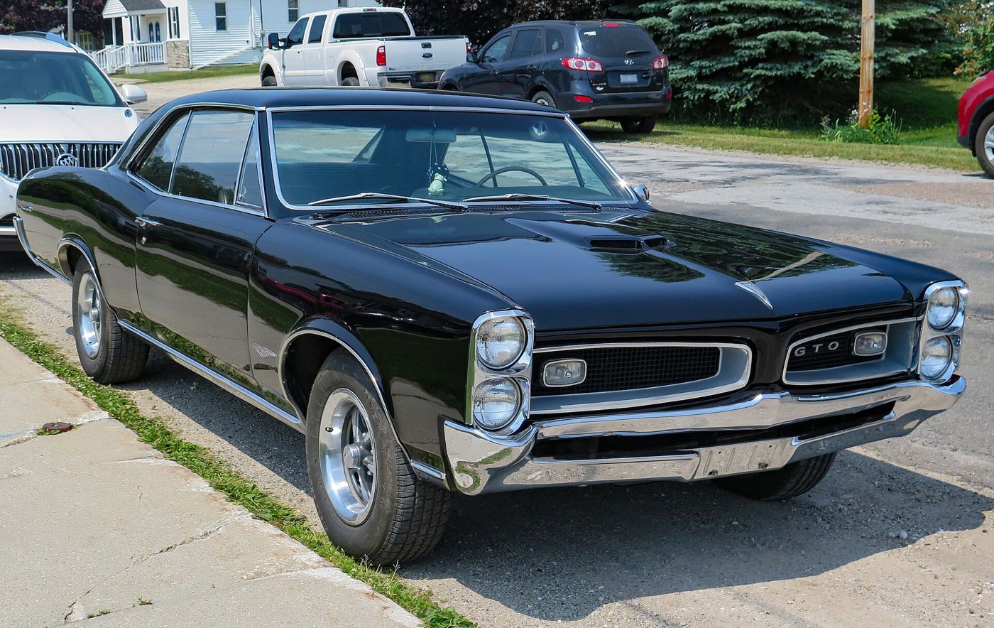 Black 1966 GTO hardtop with its recessed grilles and stacked headlamps, front three-quarter at the curb