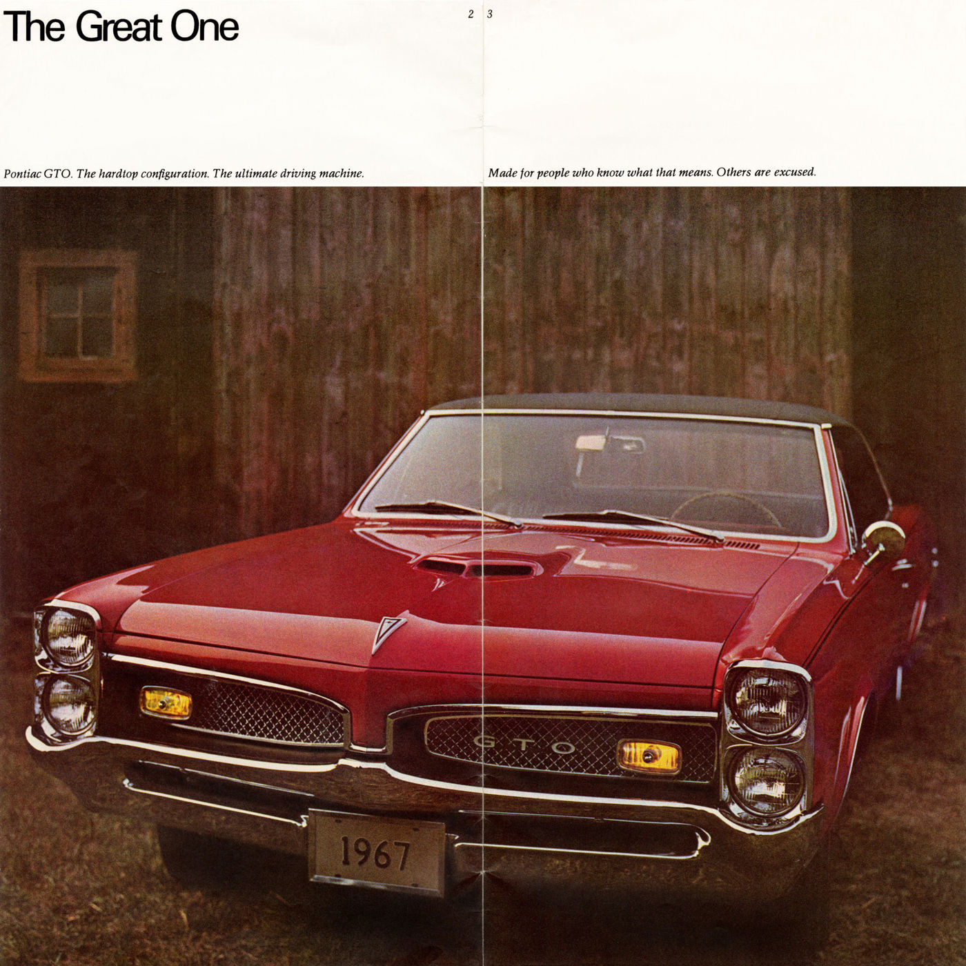 Red 1967 GTO hardtop head-on in front of a wooden barn, with its GTO grille and a 1967 display plate