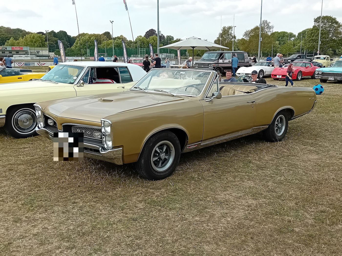 Gold 1967 GTO convertible with the top down and a mesh grille, front three-quarter on grass at a car show