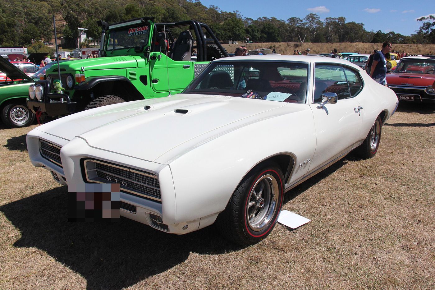 Cream 1969 GTO hardtop with split grilles and hood scoops, front three-quarter on grass at an Australian car show