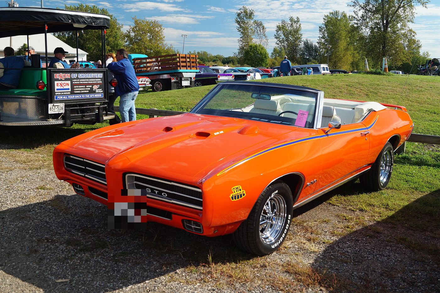 Orange 1969 GTO Judge convertible with Judge stripe and decal, top down, front three-quarter on gravel at a car show