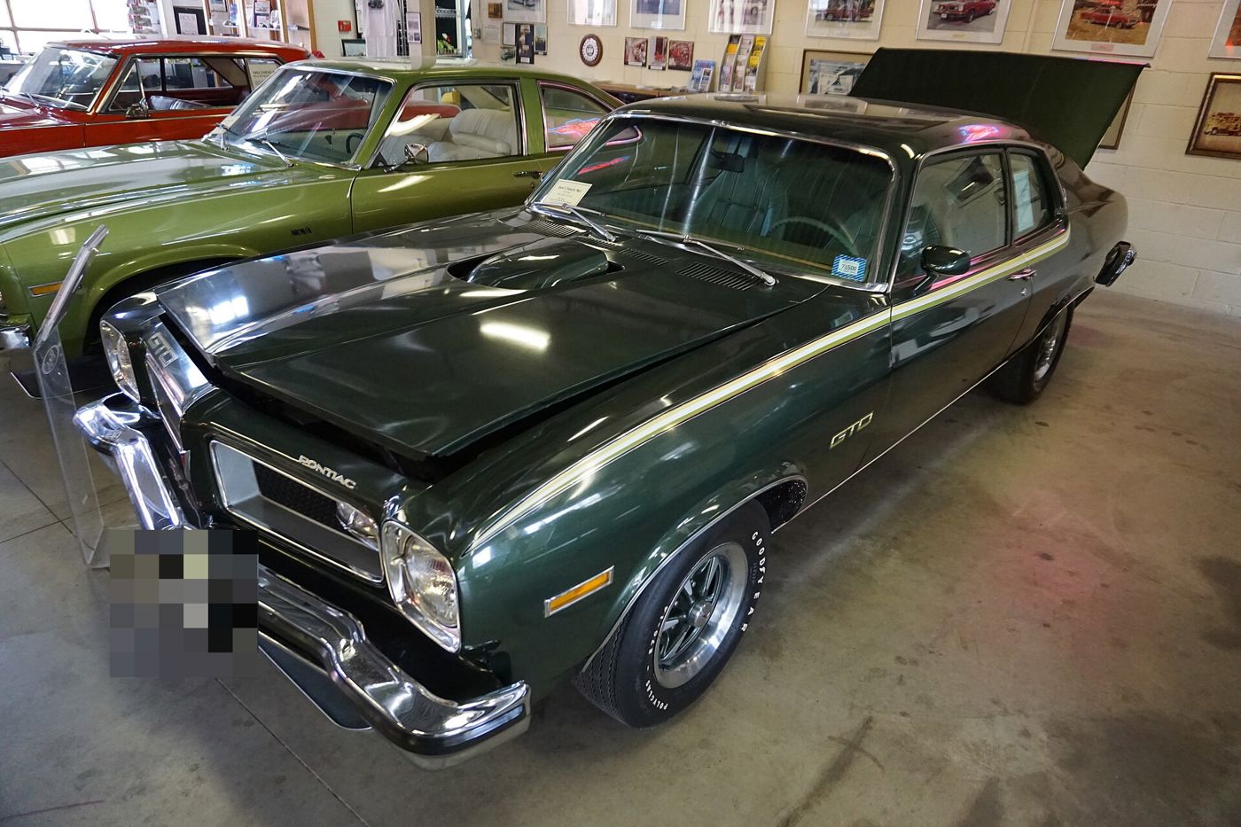 Dark green 1974 GTO with its hood up and GTO fender lettering, front three-quarter inside a museum