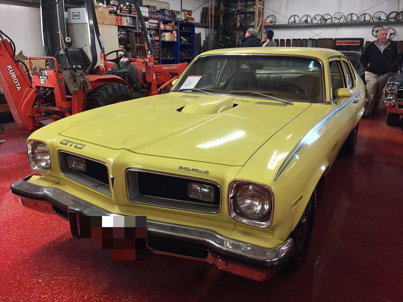 Yellow 1974 Ventura-based GTO with a shaker hood scoop and GTO lettering on the fender, front three-quarter in a garage