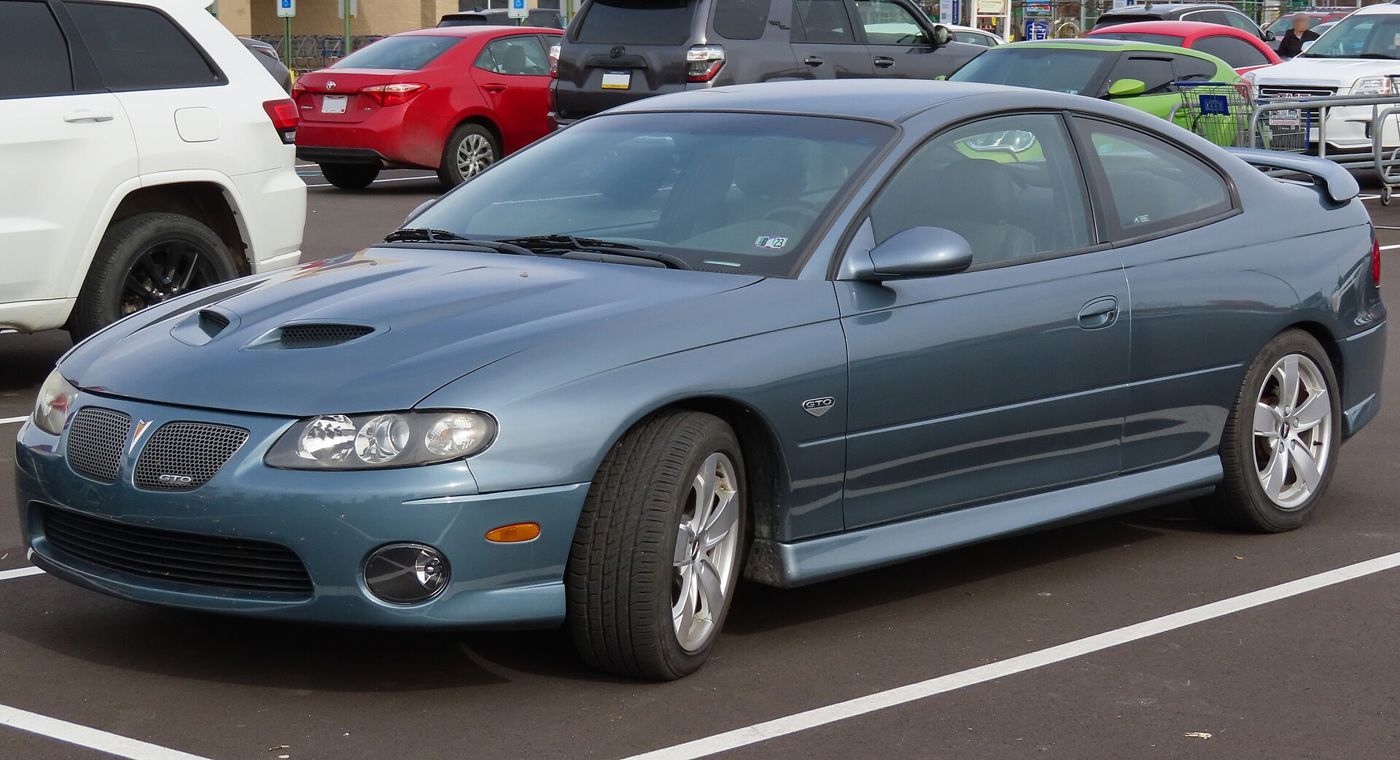 Blue-gray 2005 GTO coupe with twin hood scoops and split grille, front three-quarter in a parking lot