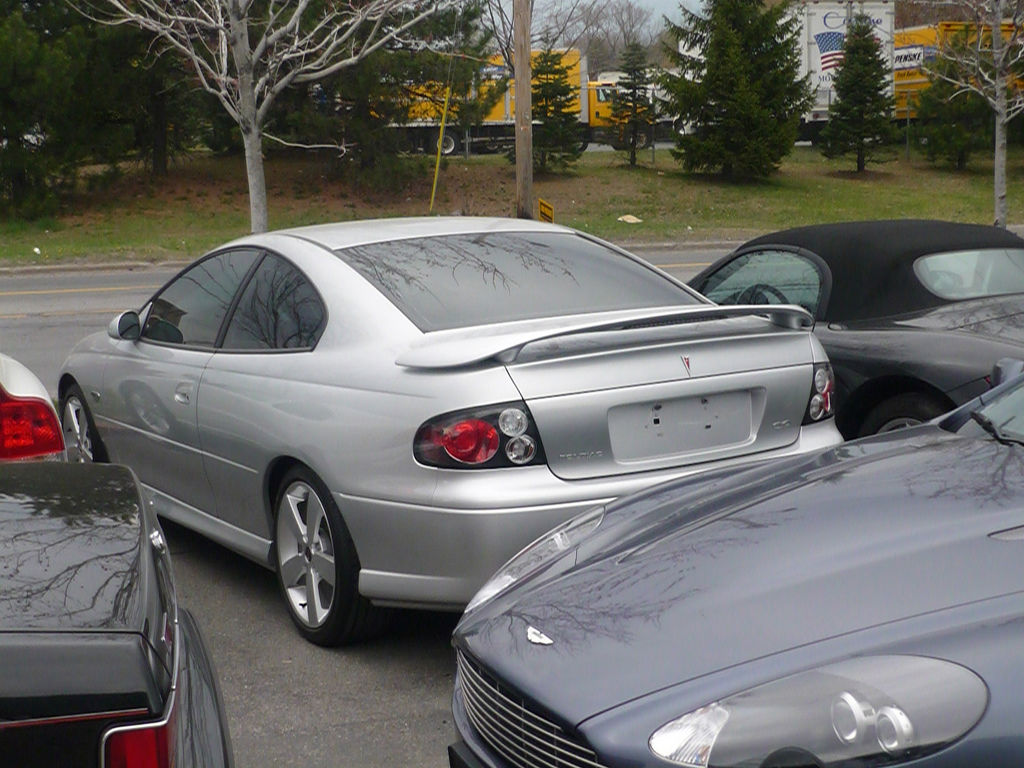 Silver 2006 GTO coupe with a decklid spoiler, rear three-quarter in a parking lot between other cars