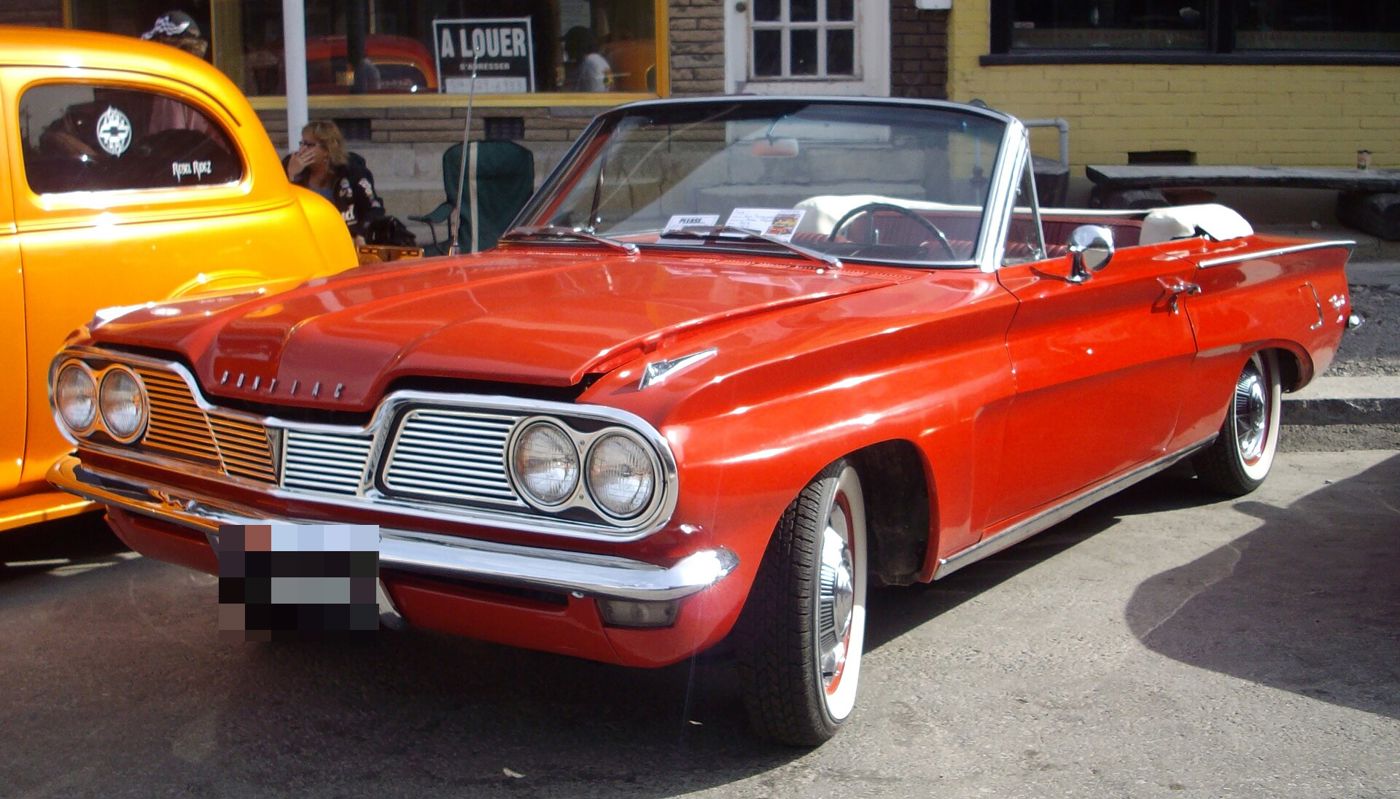 Red 1962 Tempest convertible with its top down and split grille, seen from the front three-quarter at a car show