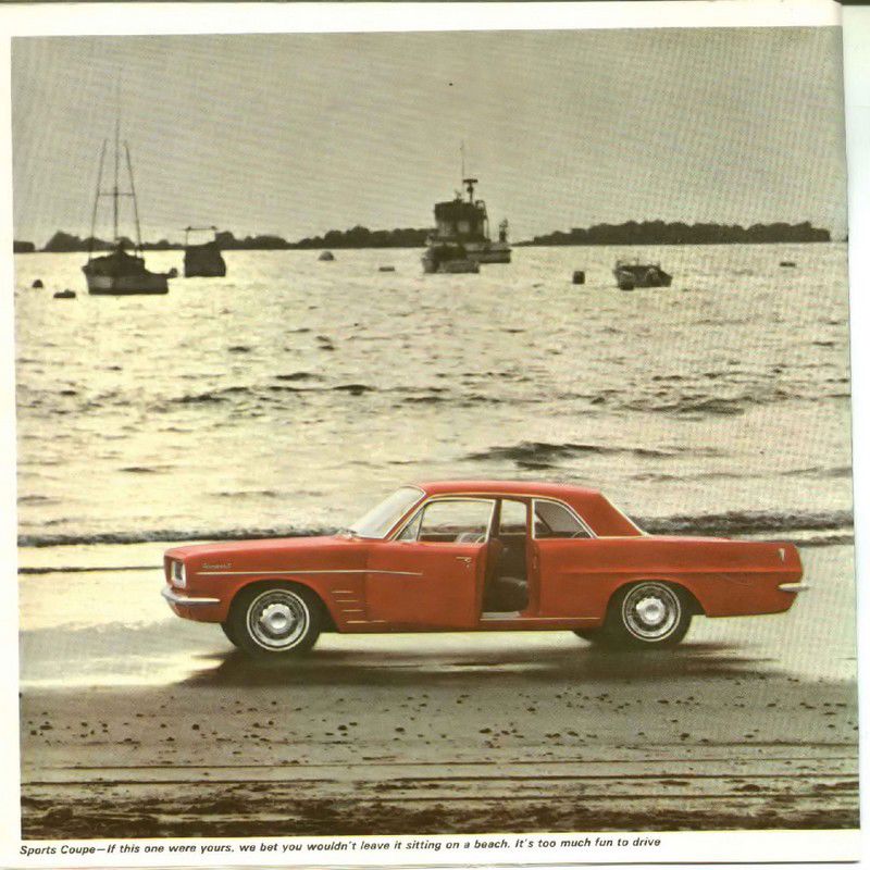 Red 1963 Tempest sports coupe with its door open, parked on sand beside the water with boats behind