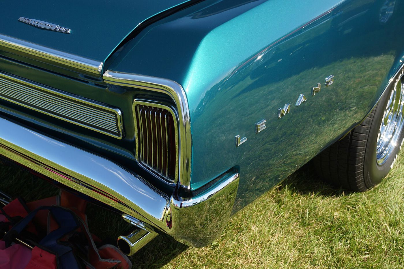 Close-up of a turquoise 1966 LeMans rear quarter panel showing the LEMANS script, the vertical-bar taillamp and chrome bumper