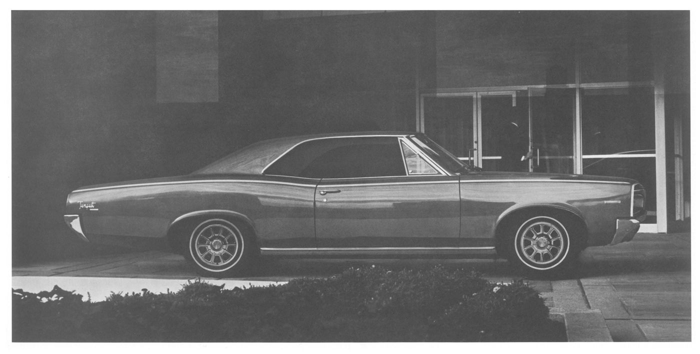 Black-and-white side view of a 1966 Tempest two-door hardtop parked in front of a glass building