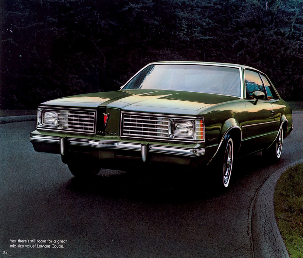 Dark green 1980 LeMans coupe with twin grilles, front three-quarter on a curving road beside trees