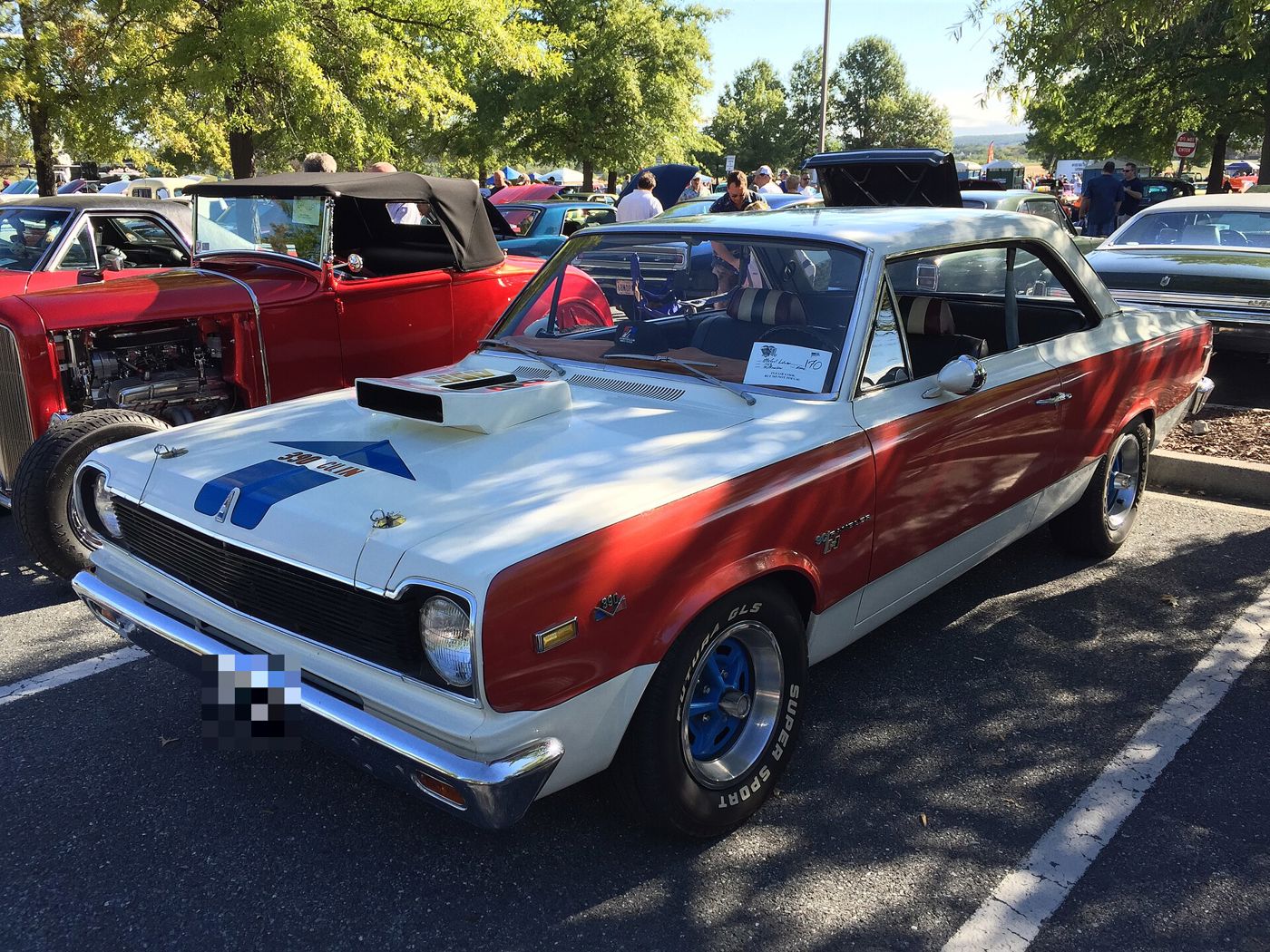 White and red 1969 SC/Rambler with blue hood arrow reading 390 CU.IN, the tall ram-air hood scoop and blue-centre wheels at a car show