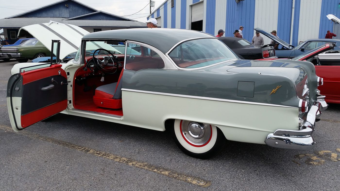 Two-tone green and cream 1955 Pontiac two-door hardtop seen from the rear three-quarter at a car show, driver's door open onto a red interior