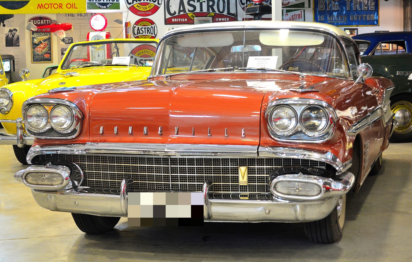 Copper-colored 1958 Pontiac Bonneville with a white roof seen head-on in a museum, showing quad headlamps, the BONNEVILLE hood lettering and the Pontiac V grille emblem