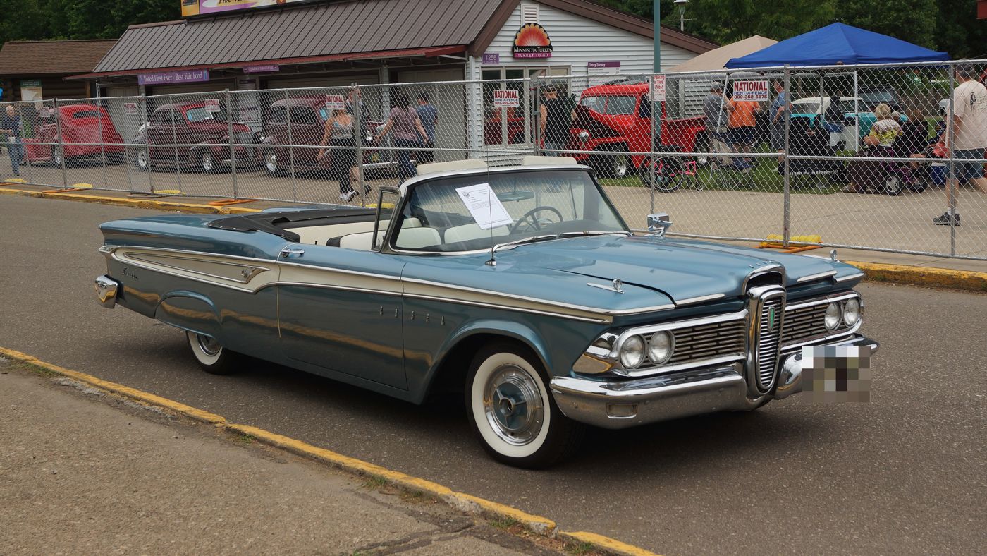 Blue 1959 Edsel Corsair convertible with the top down and white interior, in front three-quarter view at a car show, showing the 1959 split grille around the smaller vertical center