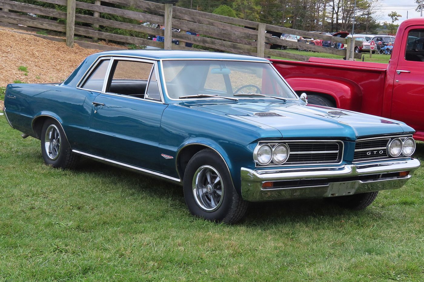 Blue-green 1964 Pontiac GTO sports coupe with stacked headlamps and GTO grille badge, front three-quarter on grass