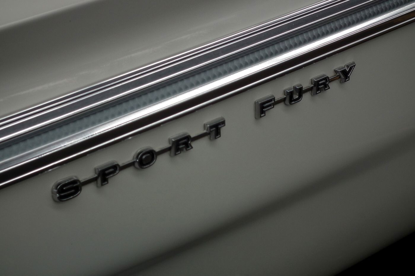 Close-up of chrome SPORT FURY block letters below a ribbed chrome side molding on a pale 1964 Plymouth
